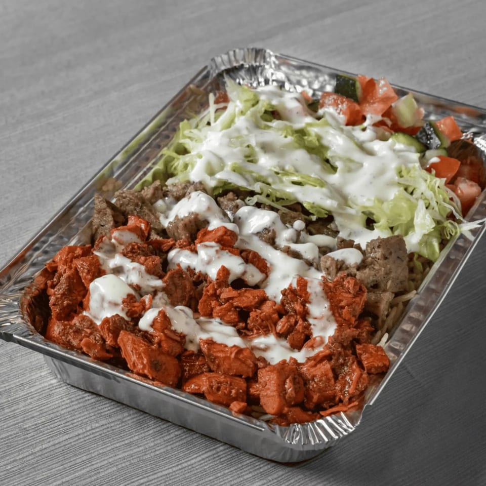 Mediterranean chicken and beef shawarma with lettuce, tomatoes, and white sauce in a foil container.
